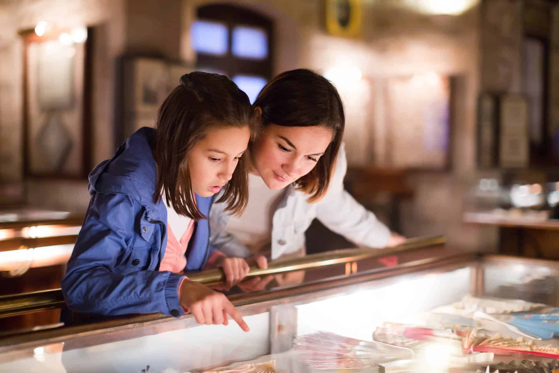 Cheerful mom and daughter looking at medieval expositions in museum