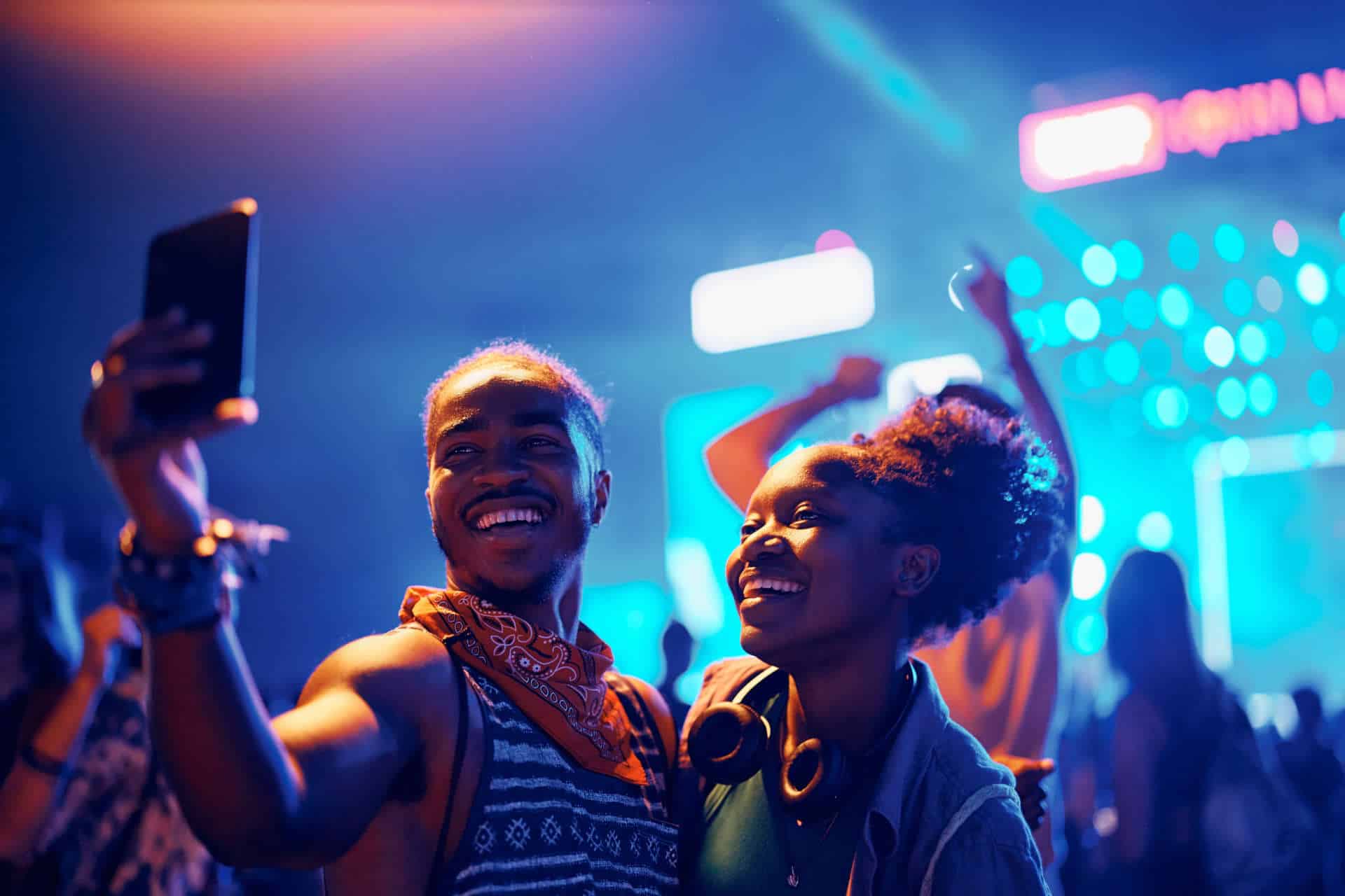 Happy couple having fun and taking selfie during summer music festival at night.