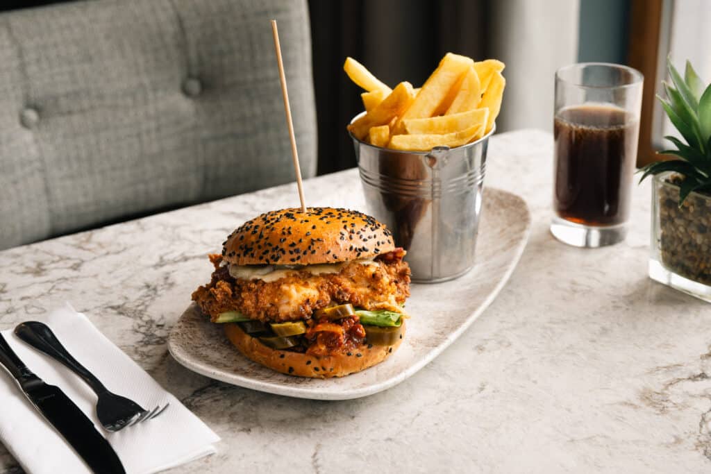Chicken burger with cheese and crispy fries served on a white marble table
