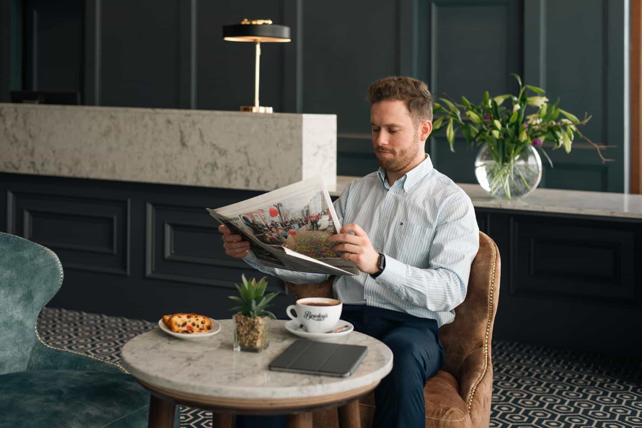 Man sitting in Viking Hotel lobby reading a newspaper with coffee and pastry on the table.